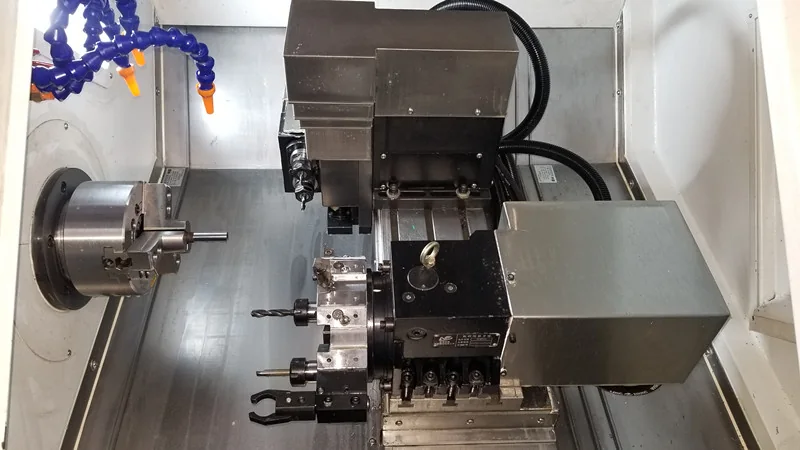 Chuck holding a small workpiece beside tool stations inside a CNC lathe