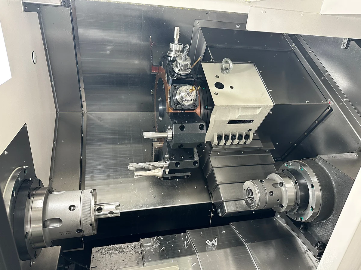 Lathe work area showing turret tools, two chucks and a cylindrical workpiece